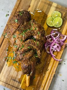 a wooden cutting board topped with meat next to sliced onions and lime wedged in half