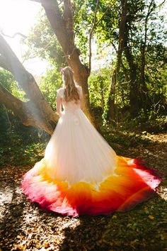 a woman in a white dress standing next to a tree and wearing a colorful skirt