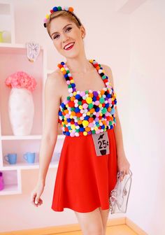 a woman in a red dress is holding a bag and wearing a necklace with multicolored balls on it