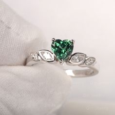 a green heart shaped diamond ring on top of a white cloth with diamonds around it