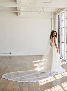 a woman in a white wedding dress standing on a wooden floor with her veil blowing in the wind