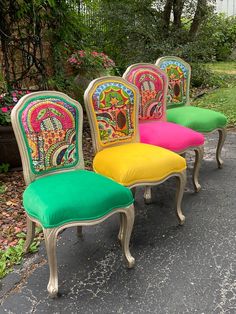 four chairs with different colored upholstered back and sides sitting in front of some bushes