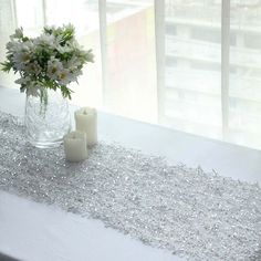 a vase with flowers and candles sitting on a table next to a window covered in silver sequins