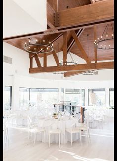 a large room with white tables and chairs, lights on the ceiling and chandeliers hanging from the rafters