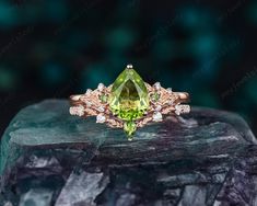 an engagement ring with green and white stones on top of a stone slab in front of a dark background