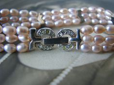 "A beautiful vintage three strand pink rice pearl beaded bracelet made by Gruen. The pearls each measure about 5.5mm x 4mm. They are spaced and tightened by chevron three hole spacer beads. The bracelet measures 1/2'' wide and 7 1/2'' long. The clasp is encrusted with Austrian crystals. In excellent \"New, Never Worn\" condition with a little patina on the silver plate ONLY DUE TO AGE, NOT WEAR. Would make a beautiful wedding bracelet. *SEE MY OTHER LISTING FOR THE MATCHING WATCH!" Vintage Round Pearl Bracelet Gift, Vintage Pink Wedding Bracelets, Vintage White Pearl Bracelet With Round Beads, Vintage Metal Pearl Bracelet For Gift, Vintage Multi-stone Wedding Bracelets, Pink Rice, Wedding Locket, Art Deco Locket, Pink Pearl Bracelet