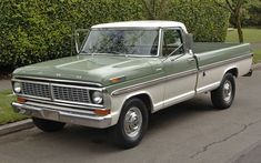 an old pick up truck is parked on the side of the road in front of some bushes