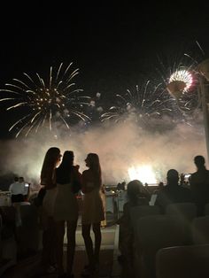 two women standing next to each other with fireworks in the sky behind them at night