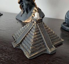 a statue is sitting on a table next to a figurine that looks like an egyptian pyramid