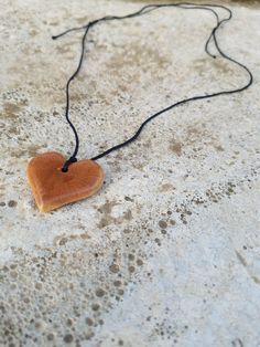 a heart shaped wooden object on a black cord attached to a stone surface with water droplets