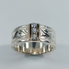 a white gold ring with two diamonds on the side and an engraved design in the middle