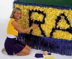 a woman sitting on the ground next to a large cake with letters painted on it