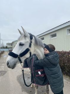 a woman standing next to a white horse wearing a black harness on it's head