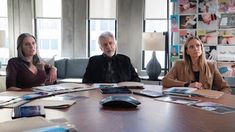 three people sitting around a table with papers on it