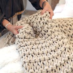 a person is making a knitted blanket out of yarn on a bed with white fur