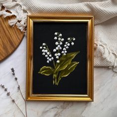 a painting with flowers in a gold frame on a marble countertop next to dried plants