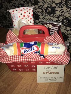 a red basket filled with lots of food on top of a wooden floor next to a sign