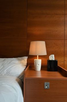 a night stand with a lamp on it next to a bed