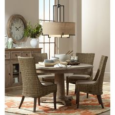 a dining room table with chairs and a large clock on the wall behind it in front of a window