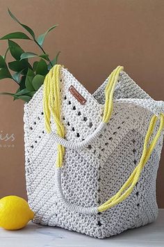 a white crocheted bag with yellow handles next to a lemon on a table