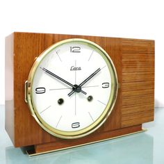 a wooden clock with white face and black hands sitting on a glass table next to a wall