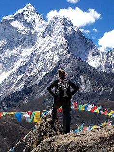 a person standing on top of a mountain looking at the mountains with prayer flags in front of them