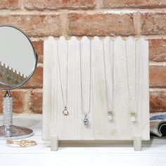 a mirror and some necklaces on a white table next to a brick wall with a book