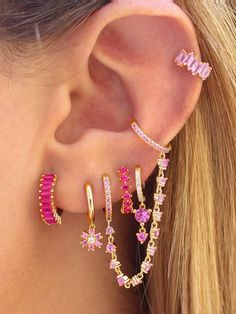 a woman wearing three pairs of pink and gold ear climbrs with diamonds on them