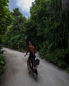 a man riding a bike down a dirt road next to lush green trees and bushes