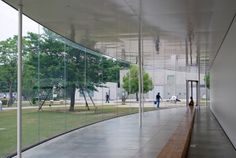 people are walking on the sidewalk in front of a large glass wall that is reflecting trees and buildings