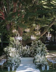 an outdoor ceremony setup with white flowers and greenery on the aisle, surrounded by tall trees