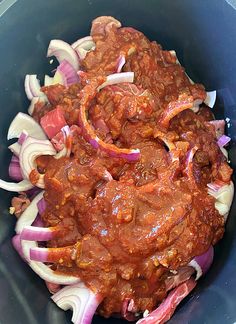 a bowl filled with meat and onions on top of a wooden table next to a knife