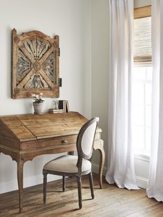 a wooden desk sitting in front of a window next to a white chair with a plant on it