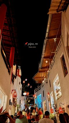 people sitting at tables in an alleyway with lights hanging from the ceiling above them