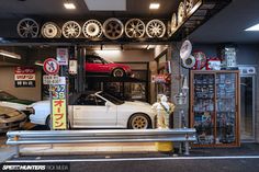 a white car is parked in front of a garage with other cars on the rack