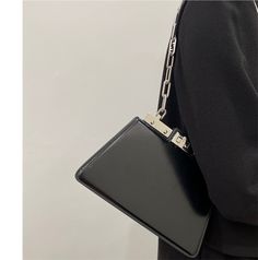 a person wearing a black jacket and holding a black purse with a chain attached to it