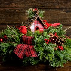 a birdhouse decorated with pine cones, red berries and evergreen needles sits on a table