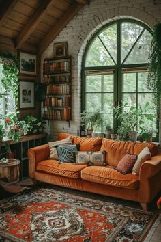 an orange couch sitting in front of a window next to a rug and potted plants