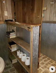 a toilet and some shelves in a room with corrugated walls on both sides, one shelf holding several rolls of toilet paper