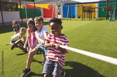 several children are playing baseball on the grass in a school yard with colorful play structures behind them