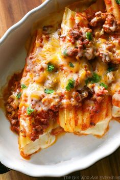 a white plate topped with lasagna shells covered in cheese and meat sauce on top of a wooden table