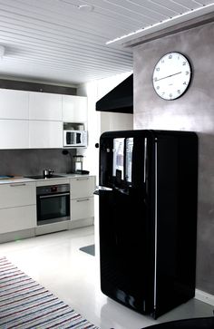 a black refrigerator sitting in the middle of a kitchen next to a clock on the wall