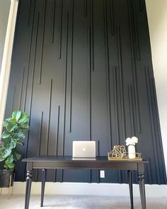 a desk with a laptop on it next to a potted plant in front of a black paneled wall