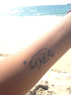 a person with a bear tattoo on their arm at the beach and water in the background