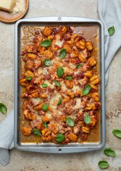 a pan filled with pasta and sauce on top of a table next to slices of bread