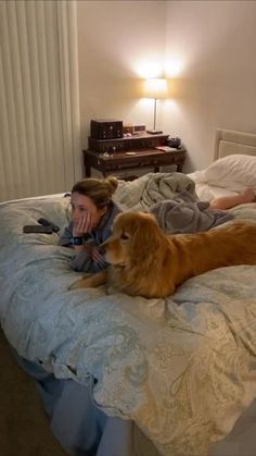 a woman laying in bed next to a dog on top of a bed with sheets