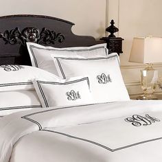 a white bed with black trim and monogrammed pillows on it, along with two night stands