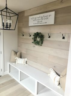 a white bench sitting under a light fixture next to a wall mounted shelf with wreaths on it