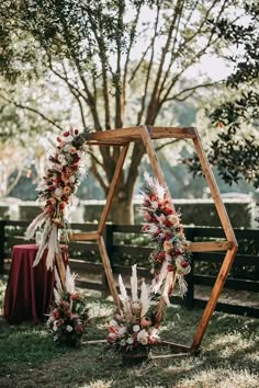 an outdoor ceremony setup with flowers and feathers on the arch, in front of a tree