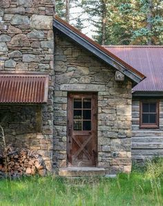 an old stone building with a door and window on the outside, surrounded by tall grass